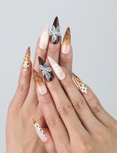 Hand model showing stiletto nails with bold brown leopard print, matte black accents, and delicate floral designs